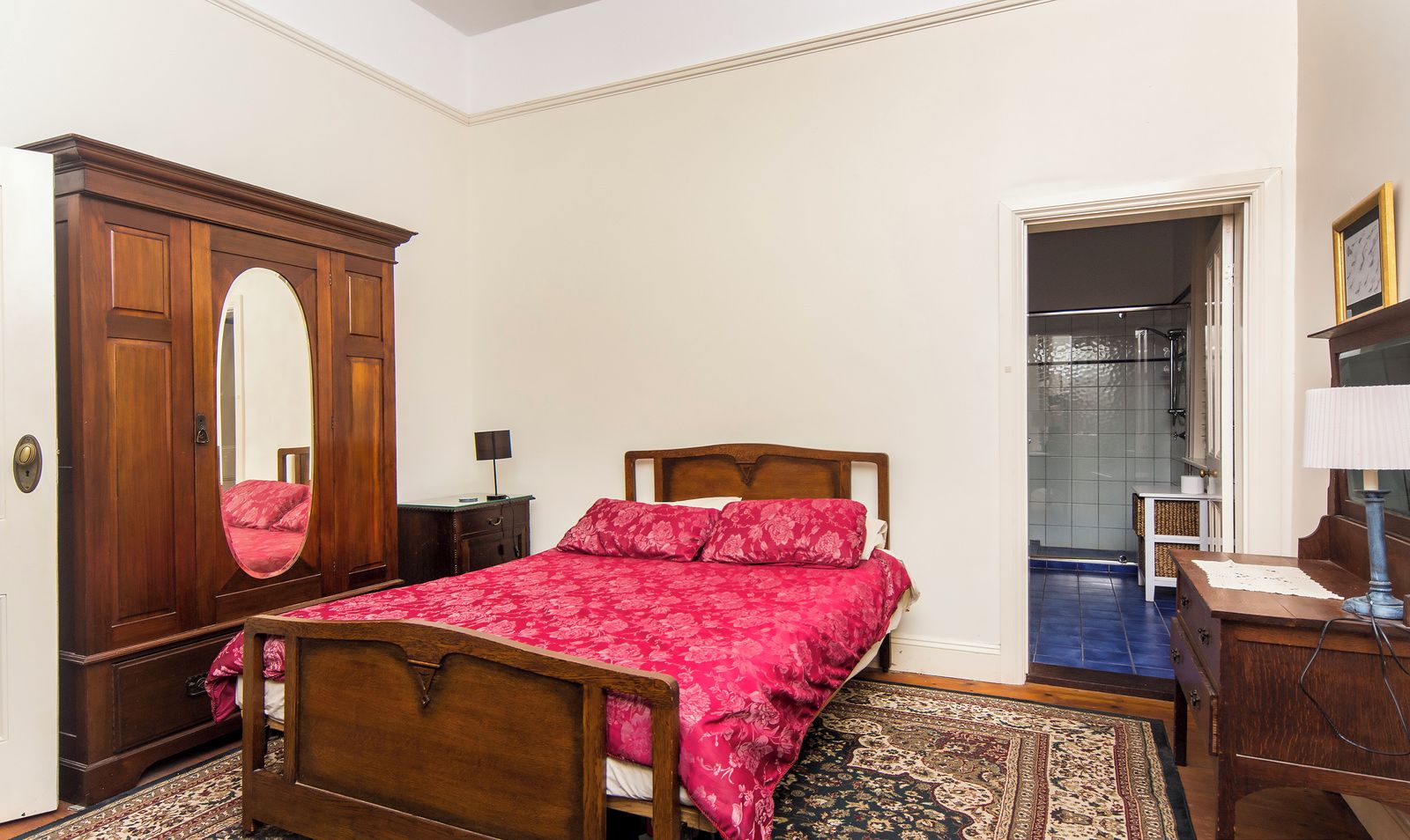 A bedroom with a wooden bed, a large mirror, a wardrobe, and a bathroom visible through an open door.