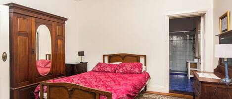 A bedroom with a wooden bed, a large mirror, a wardrobe, and a bathroom visible through an open door.