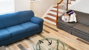 En stue med en blå sofa, en mønstret sofa, et sofabord i glas og en trappe i træ.