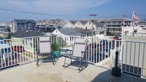 En balkon med to liggestole, en potteplante og udsigt over et boligområde med huse og parkerede biler.