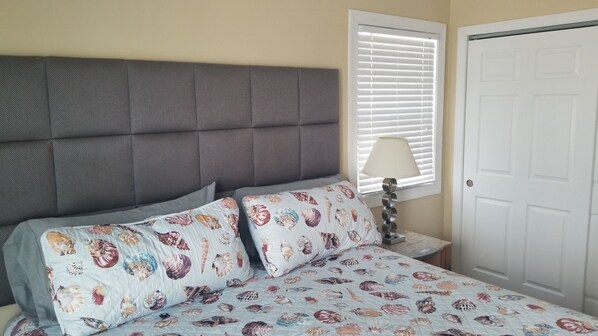 A bedroom with a tufted headboard, a bed with a floral-patterned duvet, a bedside lamp, and a window with blinds.
