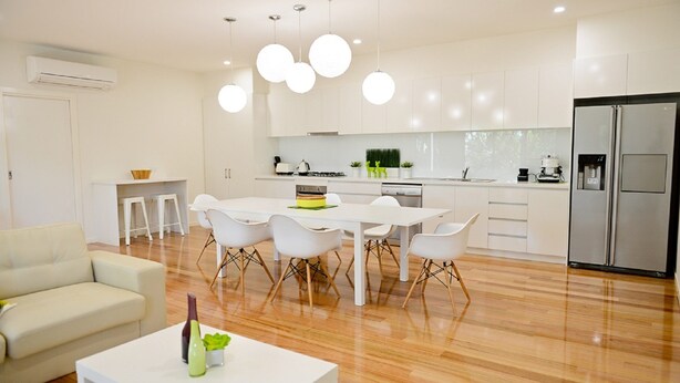 Une cuisine moderne avec des meubles blancs, une table à manger avec des chaises, un réfrigérateur et des luminaires suspendus.