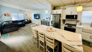 A modern kitchen with a marble countertop, a dining area with wooden chairs, a built-in oven, and a refrigerator.