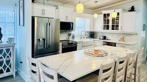 A modern kitchen with white cabinetry, a marble countertop, and a dining area with white chairs.