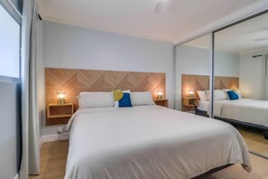 Quarto de hotel com uma cama grande, duas mesas de cabeceira com luminárias, uma cabeceira de madeira e um espelho na parede.