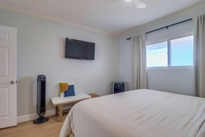 A hotel room with a bed, a flat-screen TV mounted on the wall, a bedside table with a lamp, and a window with curtains.