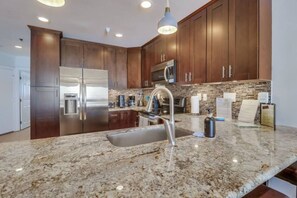 A modern kitchen with dark wooden cabinets, stainless steel appliances, granite countertops, and a built-in microwave.