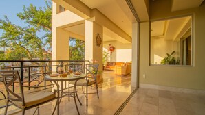 A spacious patio area with a dining table and chairs, a sofa, and a large window overlooking a garden. - Molino de Agua BEST in PV, amazing location. best pool!  Walk EVERYWHERE (Puerto Vallarta)