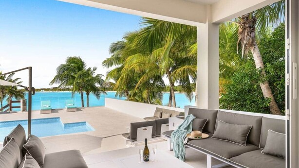A modern outdoor lounge area with a pool, seating, and a view of the ocean.