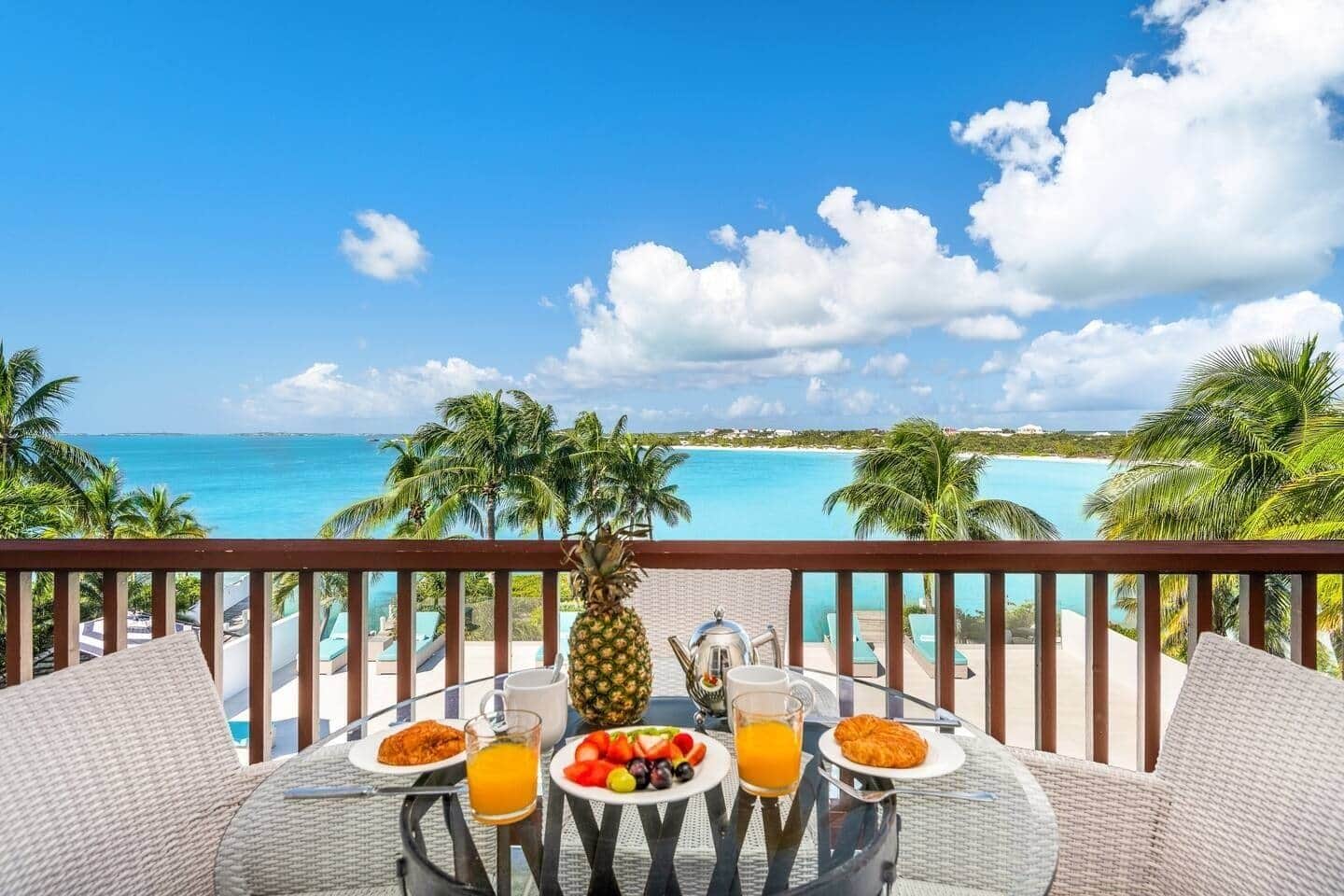 A balcony with a table set for breakfast overlooking a beach.