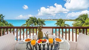 A balcony with a table set for breakfast overlooking a beach.