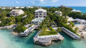 A resort with multiple overwater bungalows connected by walkways, clear turquoise water, and a view of the ocean.