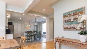 A spacious kitchen with wooden flooring, a dining area with green chairs, and a large wall clock. - Gorgeous home: walk to beach, harbor, cliff walk, wiggly bridge, dining etc. (York Harbor)