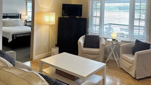 Un salon spacieux doté d’un ventilateur de plafond, d’un téléviseur et d’une grande fenêtre avec des stores.