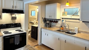 Une cuisine avec des meubles blancs, une cuisinière noire, une fenêtre donnant sur un beau paysage et un luminaire suspendu.