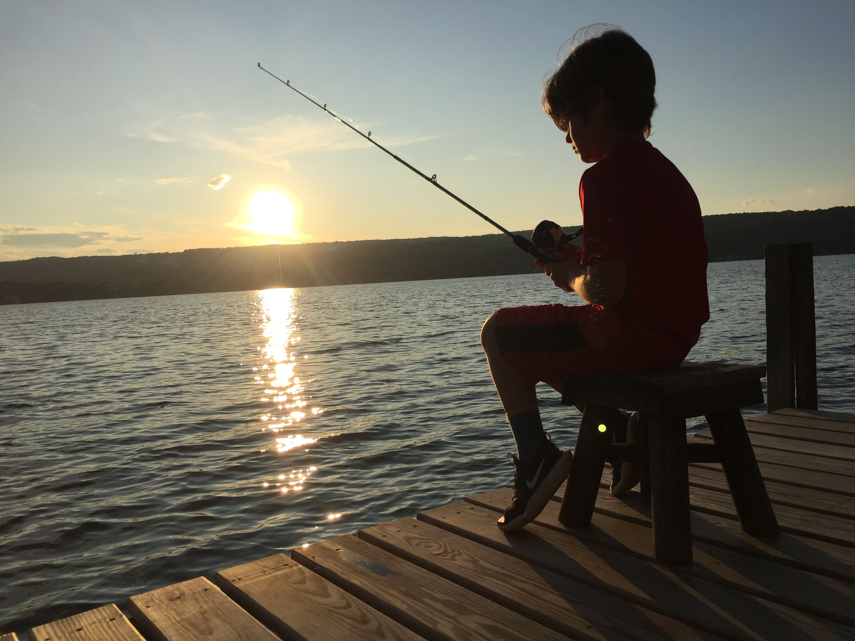 A person sitting on a wooden dock by a body of water during sunset.