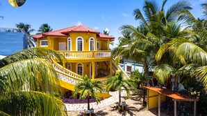 A yellow building with a red roof, surrounded by palm trees and a clear blue sky. - Luxury, Beachfront, Home with Resort-amenities, Housekeeping & FREE GOLF CART. (Hopkins)