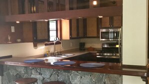Une cuisine avec un îlot central en pierre, des tabourets de bar, un four à micro-ondes et une cuisinière.