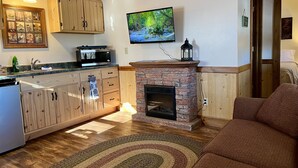 A cozy living room with a fireplace, wooden cabinets, a television, and a kitchen area with a microwave.