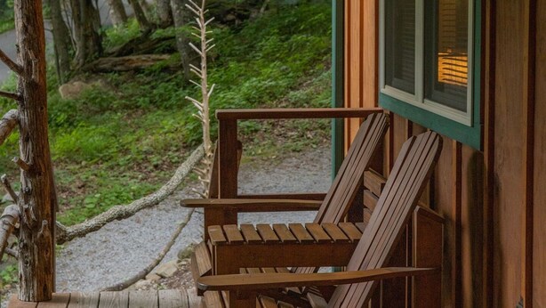 A wooden deck with two wooden chairs and a table, overlooking a forested area.