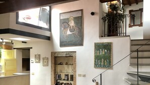 Un coin repas avec une table et des chaises en bois, une cuisine à l’arrière-plan, un escalier et un tableau accroché au mur.
