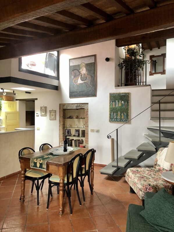 A dining area with a wooden table and chairs, a kitchen in the background, a staircase, and a painting on the wall. - Enchanting Tuscany Vacation Rental in Medieval Fortress Town Panoramic Views (Barberino Val D'elsa)
