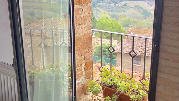Un balcon donnant sur un paysage vallonné, un mur de briques et une fenêtre avec un rideau.