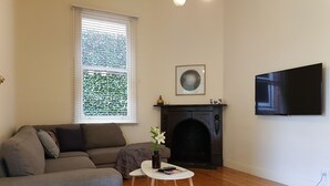 Ein Wohnzimmer mit einer Couch, einem Kamin, einem Fernseher und einem Fenster mit Jalousien.