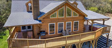 A log cabin with a balcony, a hot tub, and a grill.