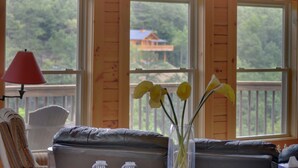 Una habitación acogedora con vistas a una casa a través de amplias ventanas, una lámpara roja y un jarrón con flores amarillas.
