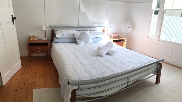En pænt redt seng med puder og et foldet håndklæde, et natbord med en lampe, og et vindue med udsigt til det fri.