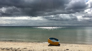 A beach with a small yellow boat on the sand, a clear view of the ocean, and a cloudy sky. - Wisteria Cottage - opposite beach (Indented Head)