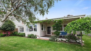 A single-story house with a covered porch, a small garden, and a lawn. - Wisteria Cottage - opposite beach (Indented Head)
