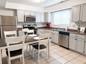 Una cocina moderna con armarios blancos, electrodomésticos de acero inoxidable y un comedor con sillas y mesa blancos.