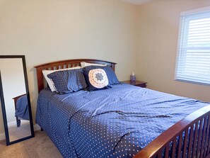 Une chambre à coucher avec un lit, une table de chevet, un miroir et une fenêtre avec des stores.