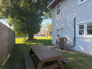 Una mesa de picnic de madera en un patio trasero, con una casa al fondo.