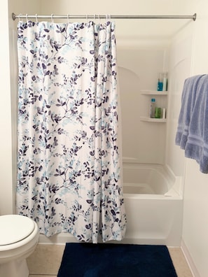 Une salle de bain avec un rideau de douche, des toilettes, une baignoire et un tapis de bain bleu.
