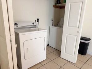 A laundry room with a washing machine, dryer, and a trash bin.