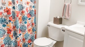 Une salle de bain avec un rideau de douche à motifs floraux, des toilettes, un lavabo et un porte-serviettes.