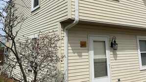 Un bâtiment à deux étages, de couleur beige, avec le numéro « 621 » affiché, une porte et un petit arbre aux fleurs blanches.
