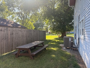 A wooden picnic table with benches in a backyard with a wooden fence and a house in the background.
