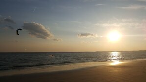 Een strand met een zonsondergang, een kalme zee en een vlieger in de lucht.