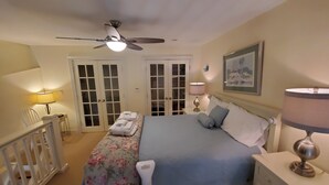 Een slaapkamer met een bed, bedlampjes, een plafondventilator, een deur met glaspanelen en een ingelijst schilderij aan de muur.