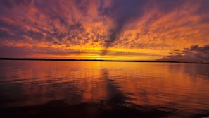 Un atardecer sobre una superficie acuática tranquila, con la silueta de una costa lejana.