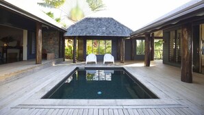 Uma área de piscina com duas cadeiras brancas, um deck de madeira e um espaço coberto para sentar, com vista para o verde.
