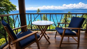 Um deck de madeira com duas cadeiras azuis acolchoadas e uma pequena mesa redonda, com vista para o oceano tropical.