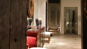 Un pasillo con una puerta de madera, un banco rojo, un banco blanco y un aparador de madera con objetos decorativos.