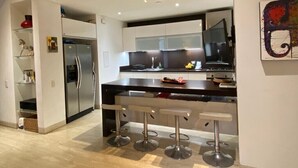 Una cocina moderna con una isla central, taburetes de bar y un refrigerador de acero inoxidable.