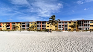 Un hôtel en bord de mer, composé de bâtiments à plusieurs étages, avec une plage de sable en premier plan et un ciel bleu dégagé.