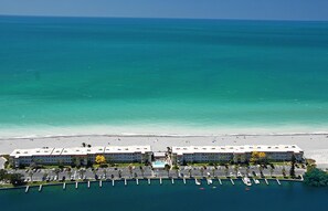 A hotel with a beachfront view, a marina with boats, and a sandy beach.